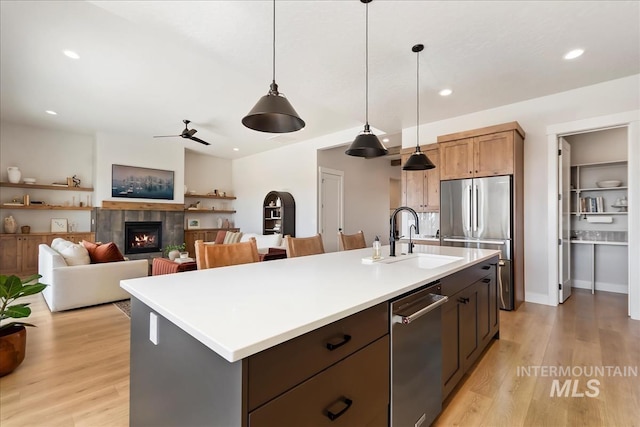 kitchen with a sink, appliances with stainless steel finishes, light wood-style floors, hanging light fixtures, and a tile fireplace