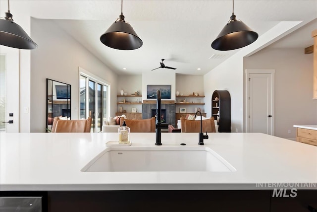 kitchen featuring a sink, ceiling fan, light countertops, pendant lighting, and open floor plan