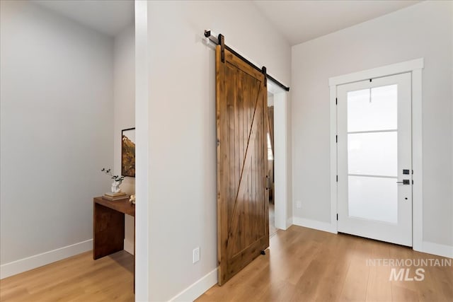 entryway with a barn door, light wood-style floors, and baseboards
