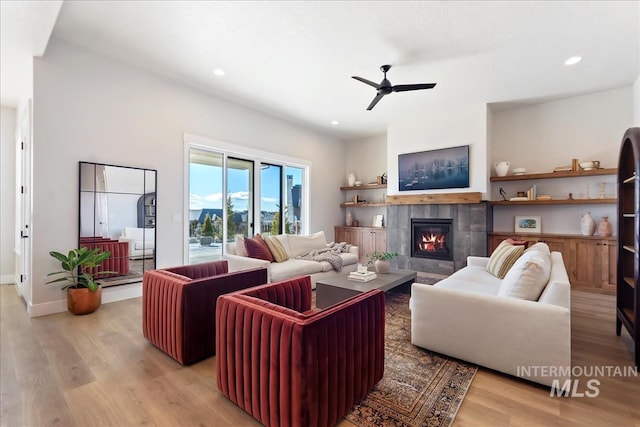living area with light wood-style floors, ceiling fan, recessed lighting, a tiled fireplace, and baseboards