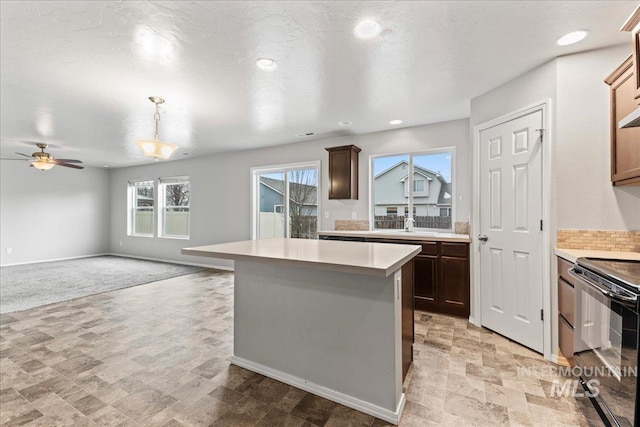 kitchen featuring black range with electric stovetop, open floor plan, light countertops, a center island, and decorative light fixtures