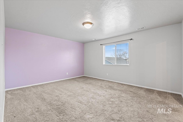 spare room with carpet, a textured ceiling, visible vents, and baseboards