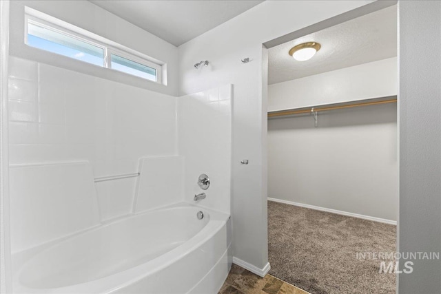 full bath with  shower combination, baseboards, a walk in closet, and a textured ceiling