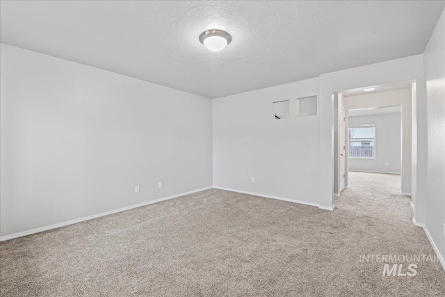 empty room with light carpet, baseboards, and a textured ceiling