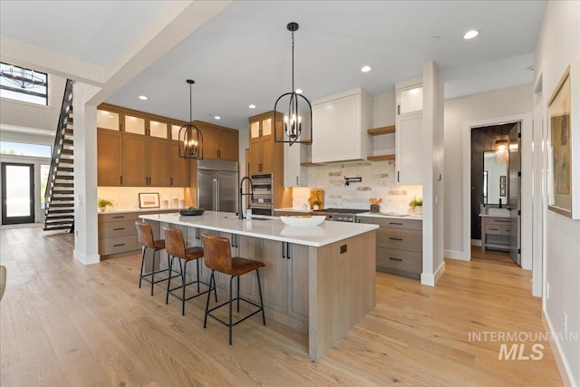 kitchen with light wood-type flooring, stainless steel appliances, a spacious island, white cabinetry, and hanging light fixtures