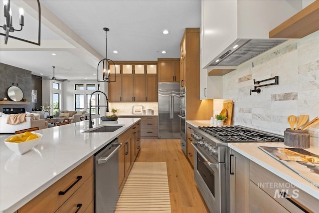 kitchen featuring high end appliances, wall chimney range hood, sink, ceiling fan, and light wood-type flooring