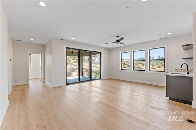 unfurnished living room featuring ceiling fan, sink, light hardwood / wood-style floors, and plenty of natural light