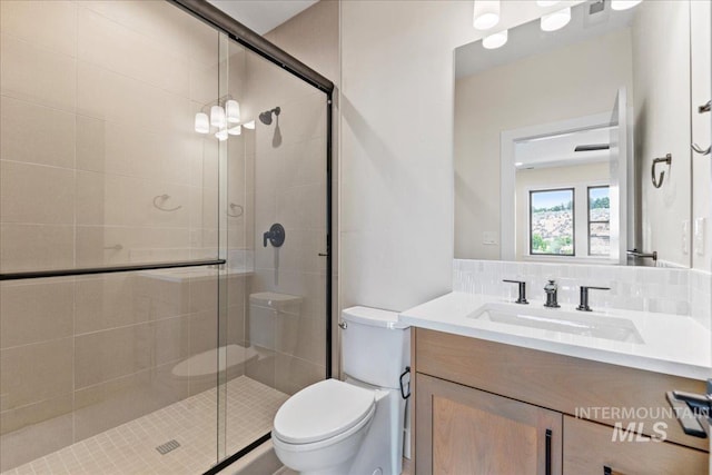 bathroom featuring vanity, an inviting chandelier, toilet, tasteful backsplash, and an enclosed shower