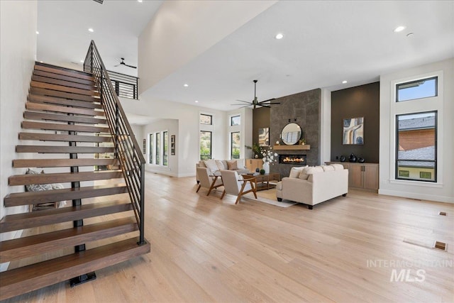 living room with ceiling fan, a large fireplace, and light wood-type flooring