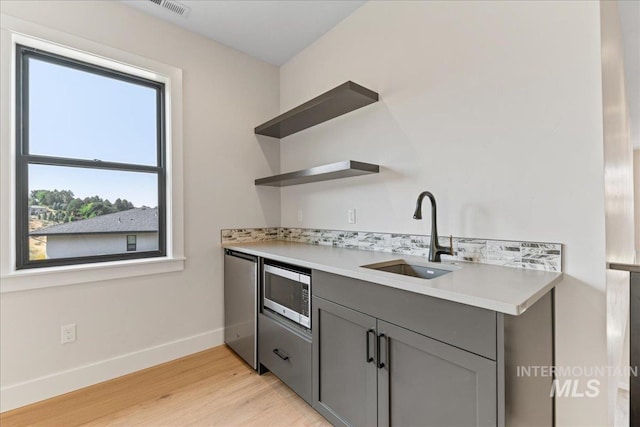 kitchen featuring stainless steel microwave, refrigerator, sink, light hardwood / wood-style flooring, and gray cabinets