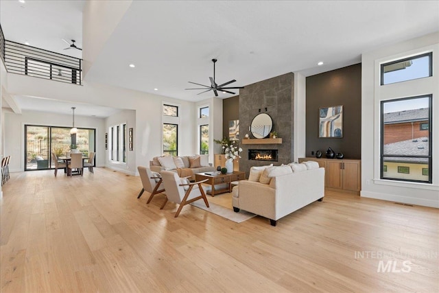 living room with light wood-type flooring, ceiling fan, and a tiled fireplace