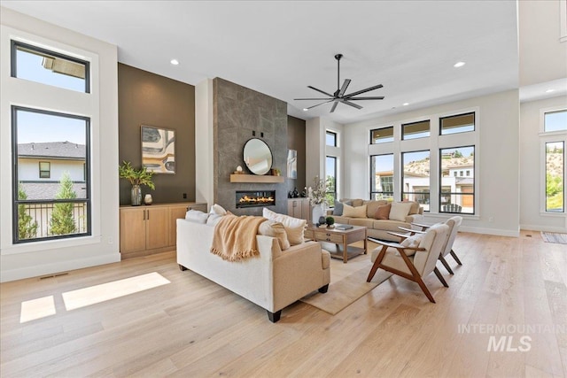 living room with light hardwood / wood-style flooring, ceiling fan, and a tiled fireplace