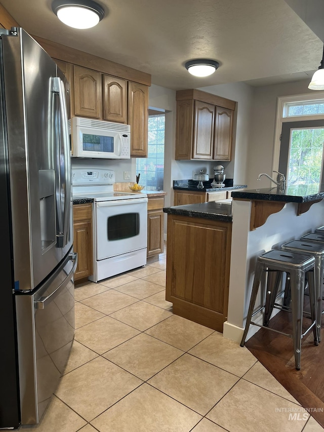 140 W Valley Rd, Hagerman, ID 83332 - kitchen featuring white appliances, a kitchen bar, light tile patterned flooring, and brown cabinetry