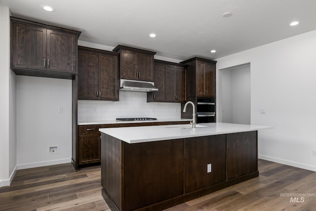 kitchen with a kitchen island with sink, stainless steel gas stovetop, sink, dark brown cabinets, and decorative backsplash