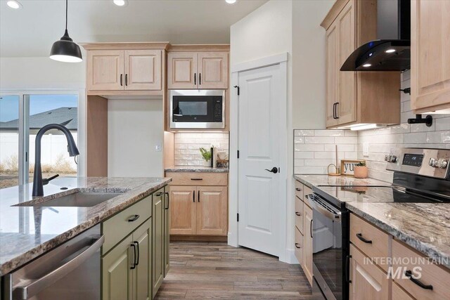 kitchen featuring wall chimney exhaust hood, sink, light stone counters, appliances with stainless steel finishes, and pendant lighting