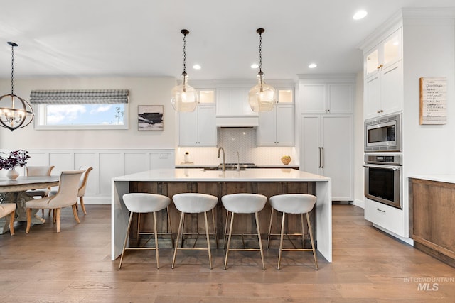 kitchen featuring a kitchen island with sink, appliances with stainless steel finishes, decorative light fixtures, light hardwood / wood-style floors, and white cabinetry