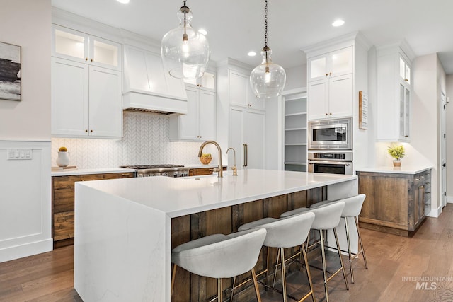 kitchen with hanging light fixtures, stainless steel appliances, dark hardwood / wood-style flooring, a center island with sink, and white cabinets