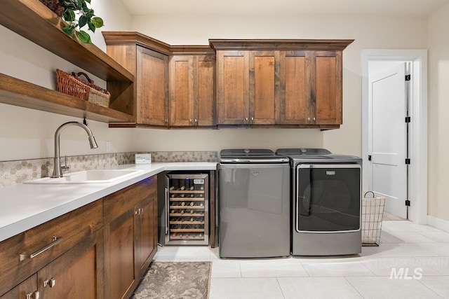 clothes washing area with sink, cabinets, beverage cooler, washer and clothes dryer, and light tile patterned flooring