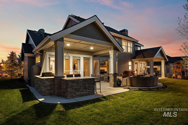 back house at dusk featuring a lawn, an outdoor living space, a patio area, and exterior bar