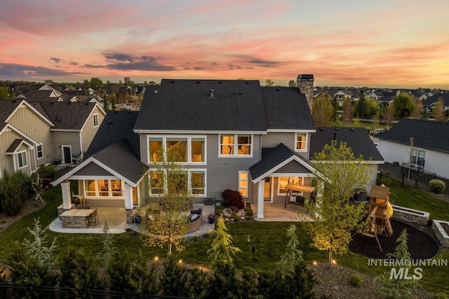 back house at dusk featuring a patio and a lawn