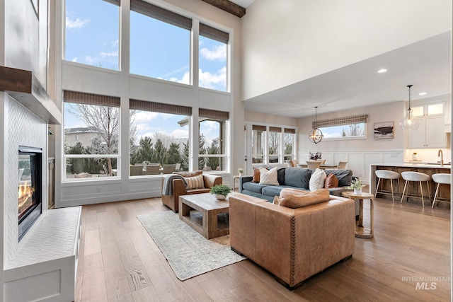 living room with sink, light hardwood / wood-style flooring, a towering ceiling, and an inviting chandelier