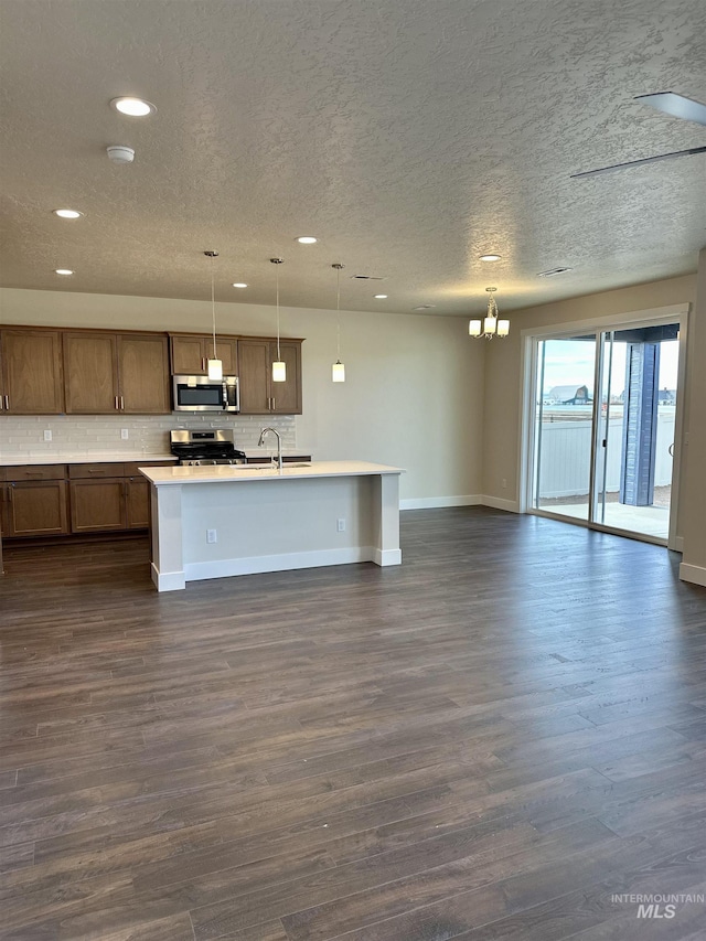 kitchen featuring pendant lighting, stainless steel appliances, a notable chandelier, a center island with sink, and dark hardwood / wood-style flooring