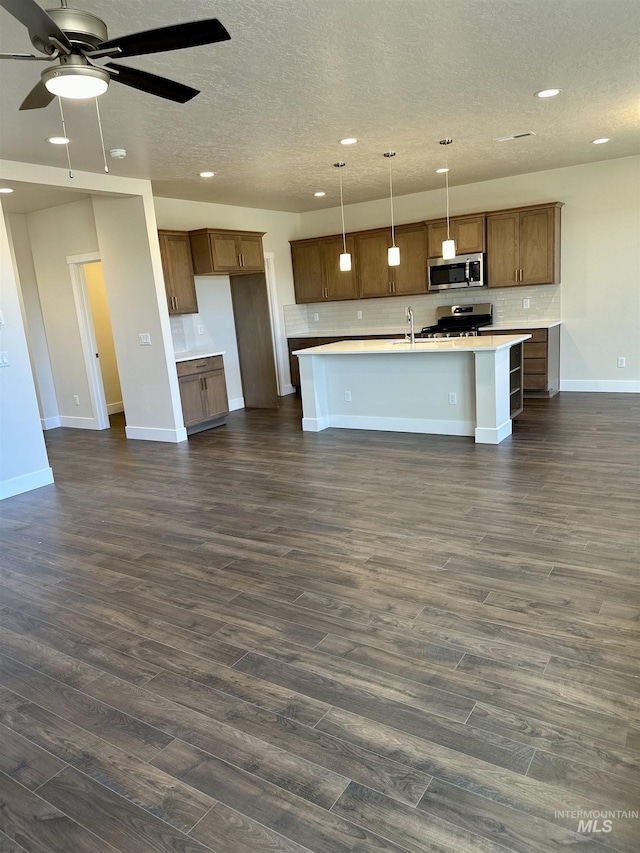 kitchen with stainless steel appliances, dark hardwood / wood-style floors, an island with sink, and hanging light fixtures