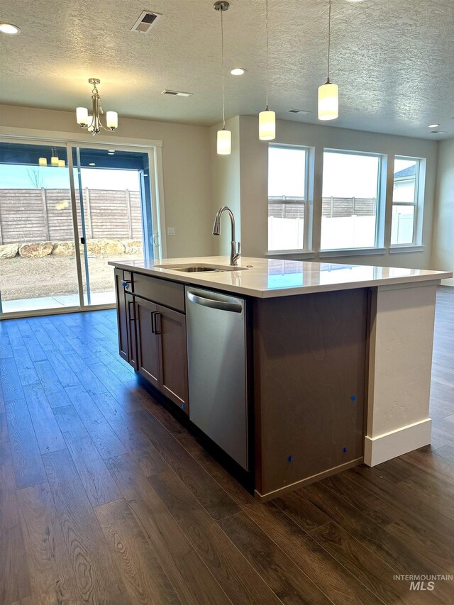 kitchen featuring pendant lighting, sink, dark hardwood / wood-style flooring, stainless steel dishwasher, and a center island with sink