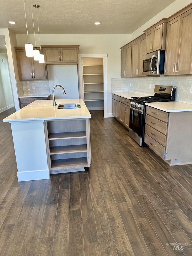 kitchen featuring a kitchen island with sink, sink, decorative light fixtures, and appliances with stainless steel finishes