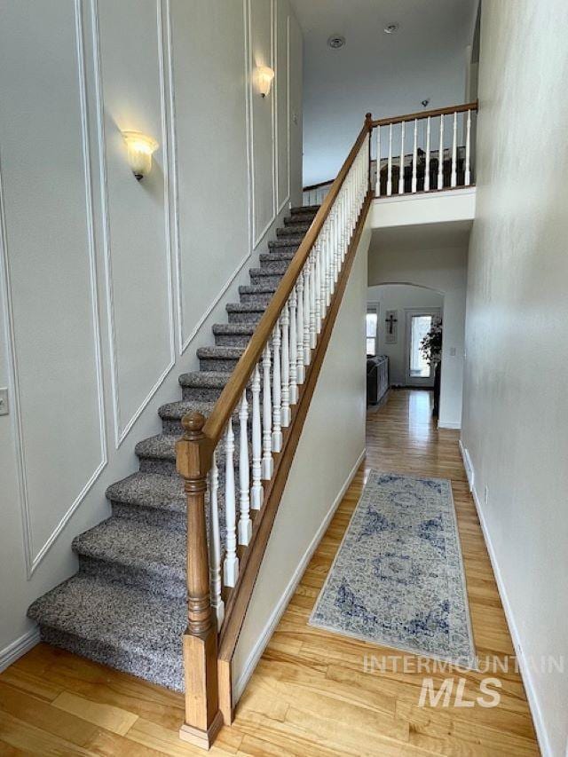 stairway with a high ceiling, wood finished floors, baseboards, and arched walkways