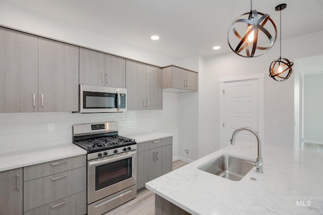 kitchen featuring decorative backsplash, appliances with stainless steel finishes, sink, light hardwood / wood-style flooring, and hanging light fixtures