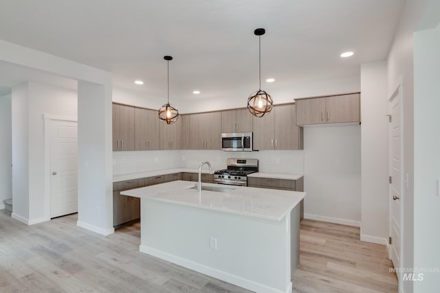 kitchen featuring pendant lighting, light hardwood / wood-style floors, a kitchen island with sink, and appliances with stainless steel finishes