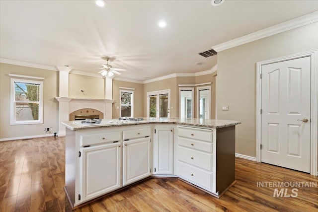 kitchen featuring white gas stovetop, light hardwood / wood-style floors, a center island, light stone countertops, and white cabinets