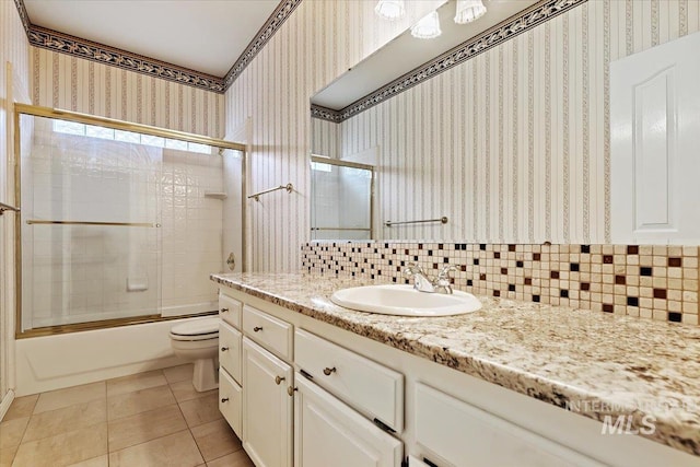 full bathroom featuring toilet, tile patterned flooring, tasteful backsplash, bath / shower combo with glass door, and vanity