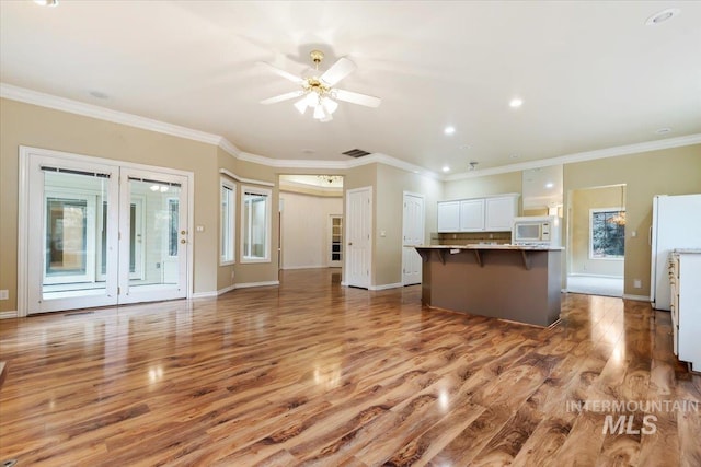 kitchen featuring white appliances, ceiling fan, ornamental molding, a kitchen bar, and white cabinetry