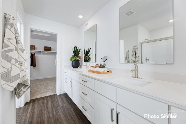 bathroom featuring wood finished floors, a shower stall, a spacious closet, double vanity, and recessed lighting