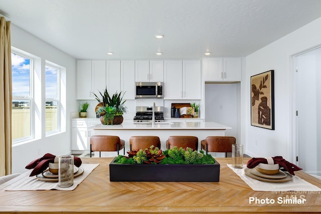 kitchen featuring stainless steel appliances, white cabinets, recessed lighting, a kitchen island with sink, and a sink