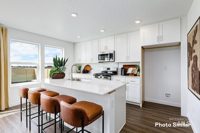 kitchen featuring a sink, stainless steel appliances, a center island with sink, dark wood-style floors, and white cabinetry
