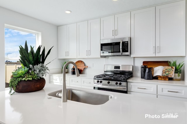 kitchen with stainless steel appliances, a sink, white cabinetry, light countertops, and recessed lighting