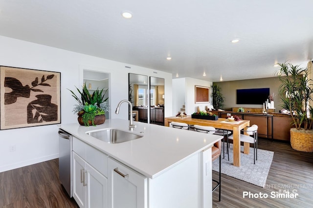 kitchen with a sink, open floor plan, a center island with sink, white cabinetry, and light countertops