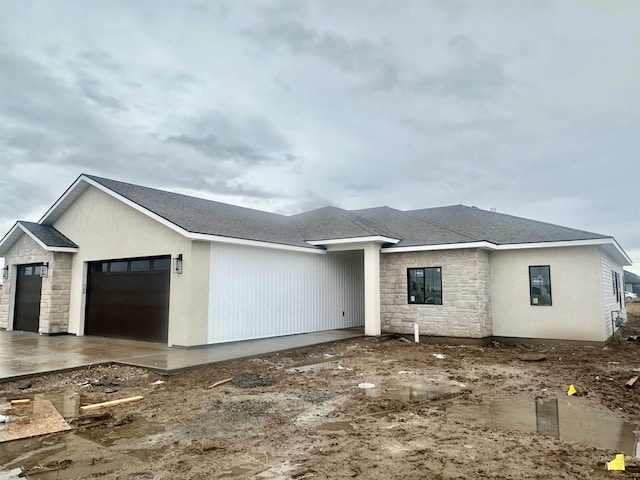 view of front of home with a garage, stone siding, and roof with shingles