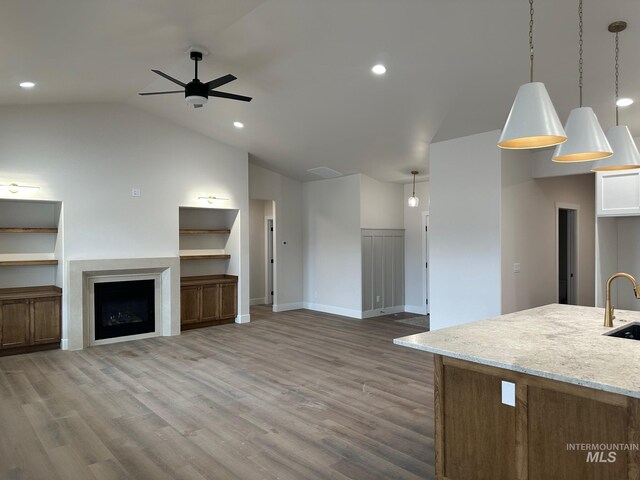 unfurnished living room featuring ceiling fan, vaulted ceiling, recessed lighting, wood finished floors, and a sink