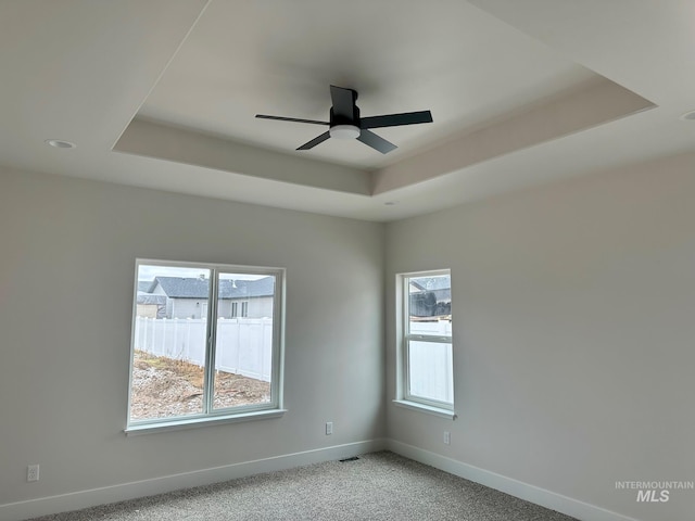 unfurnished room with visible vents, baseboards, ceiling fan, a raised ceiling, and light colored carpet