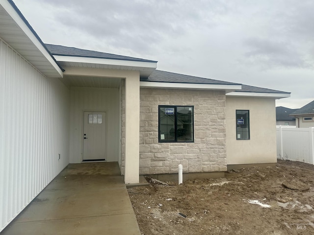 doorway to property featuring a carport, fence, stone siding, and a shingled roof