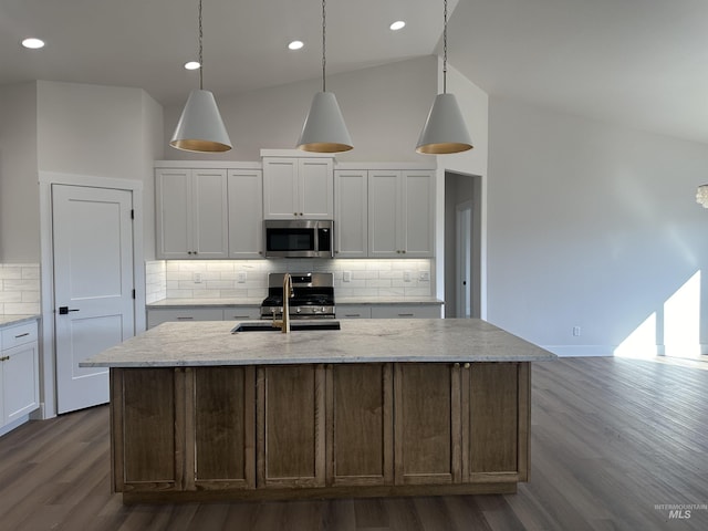 kitchen featuring stainless steel microwave, a center island with sink, backsplash, and a sink