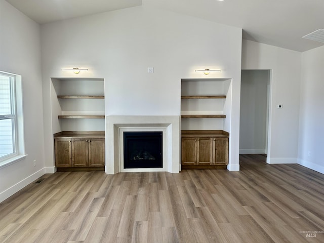 unfurnished living room featuring visible vents, wood finished floors, a fireplace, and vaulted ceiling