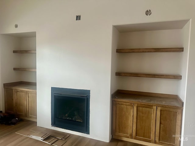 unfurnished living room featuring a glass covered fireplace and wood finished floors