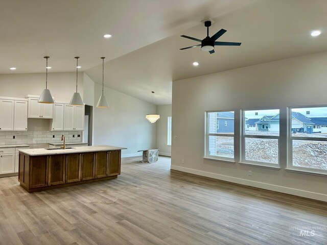 kitchen with a center island with sink, light wood finished floors, ceiling fan, decorative backsplash, and light countertops