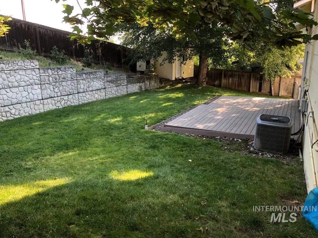 view of yard with a fenced backyard, a deck, and central AC unit