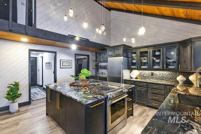 kitchen with high vaulted ceiling, light hardwood / wood-style floors, decorative light fixtures, wooden walls, and appliances with stainless steel finishes